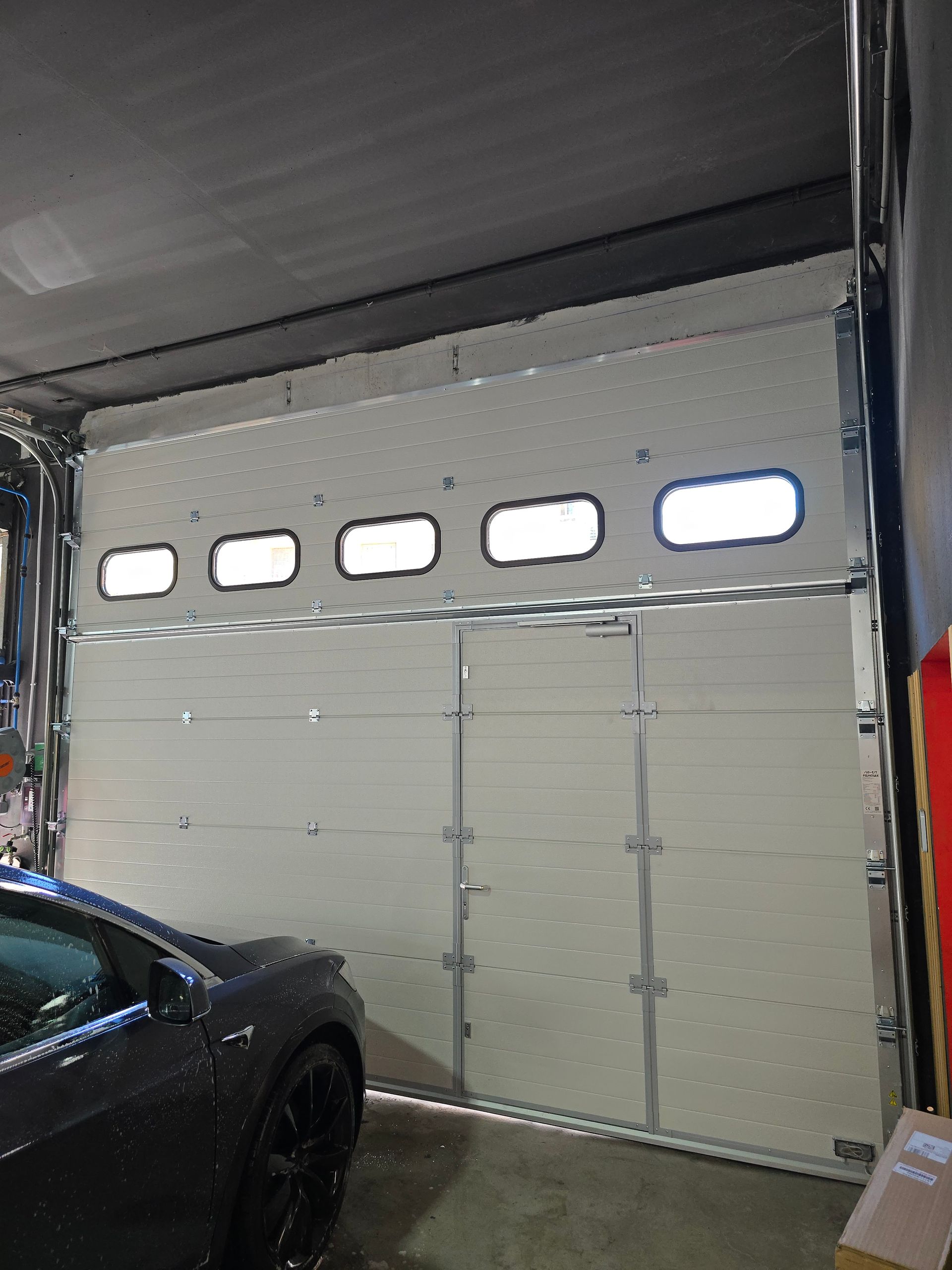 Porte de garage vitrée, partiellement ouverte, laissant apparaître une voiture à l'intérieur.