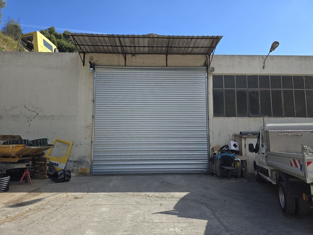 Porte sectionnelle grise sur un bâtiment en béton avec un petit auvent. Lumière du soleil.