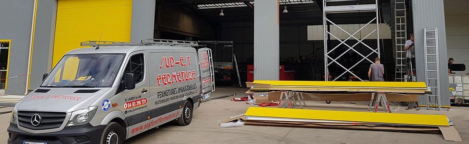 Une camionnette de chantier argentée devant un bâtiment avec un mur jaune et des échafaudages.