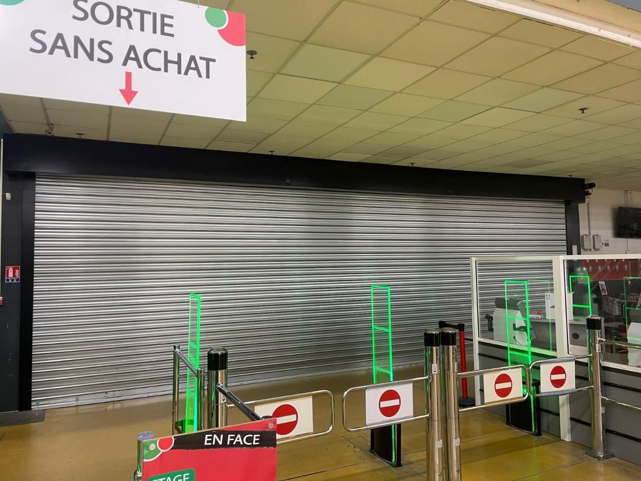 Sortie de supermarché fermée avec porte de sécurité coulissante, sans barrières d'entrée et avec un panneau « Sortie sans achat ».