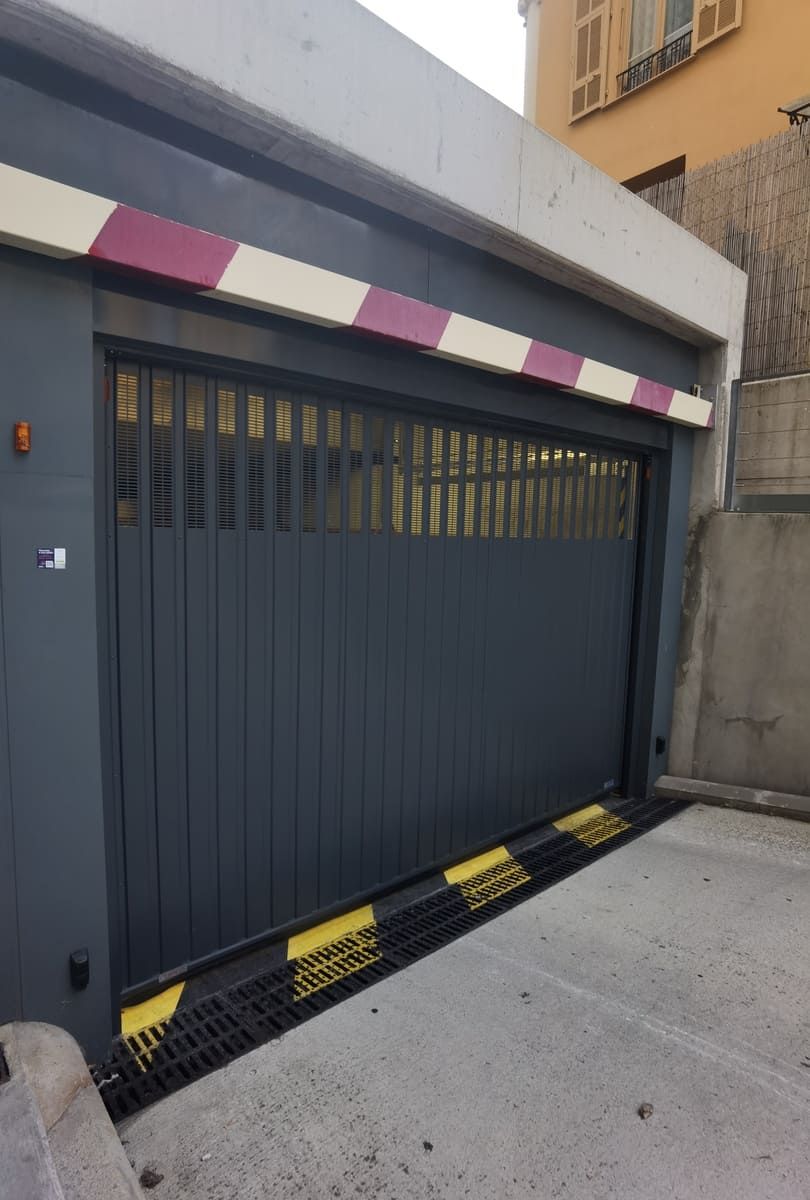 Portail de garage gris fermé avec bandes de signalisation et protections.
