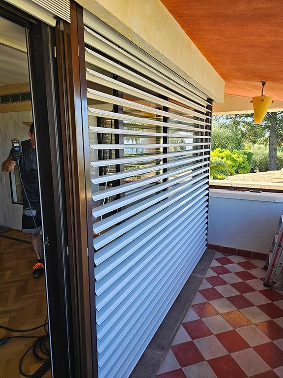 Extérieur d'un bâtiment avec des volets blancs à persiennes au-dessus d'une fenêtre, un sol carrelé en damier et un balcon.