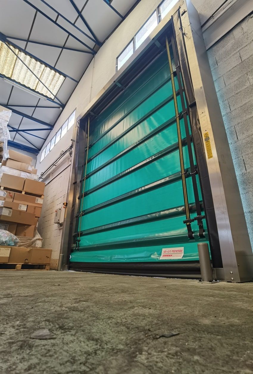 Porte industrielle verte à ouverture rapide dans un entrepôt, avec cadre en acier inoxydable, rayures noires et perspective en angle.