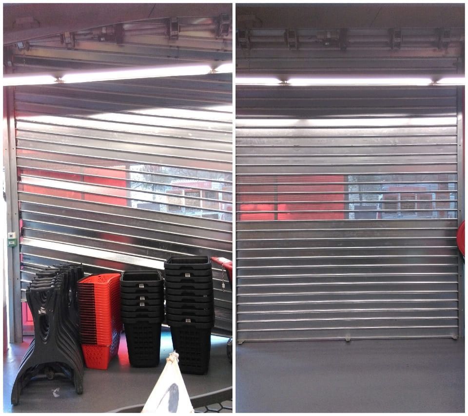 Volet de sécurité métallique endommagé. Le côté gauche est tordu, le côté droit semble en bon état. À l'intérieur d'un magasin.