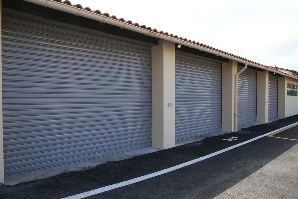 Rangée de portes sectionnelles grises sur un bâtiment avec une allée pavée et un toit de tuiles.