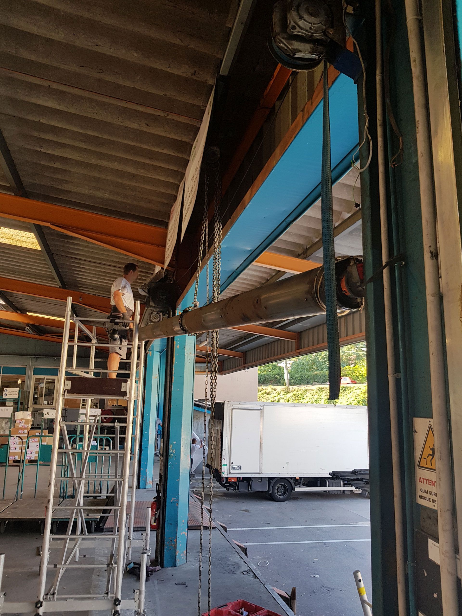 Un homme répare le mécanisme d'une porte de garage sectionnelle sur un échafaudage. Atelier extérieur.