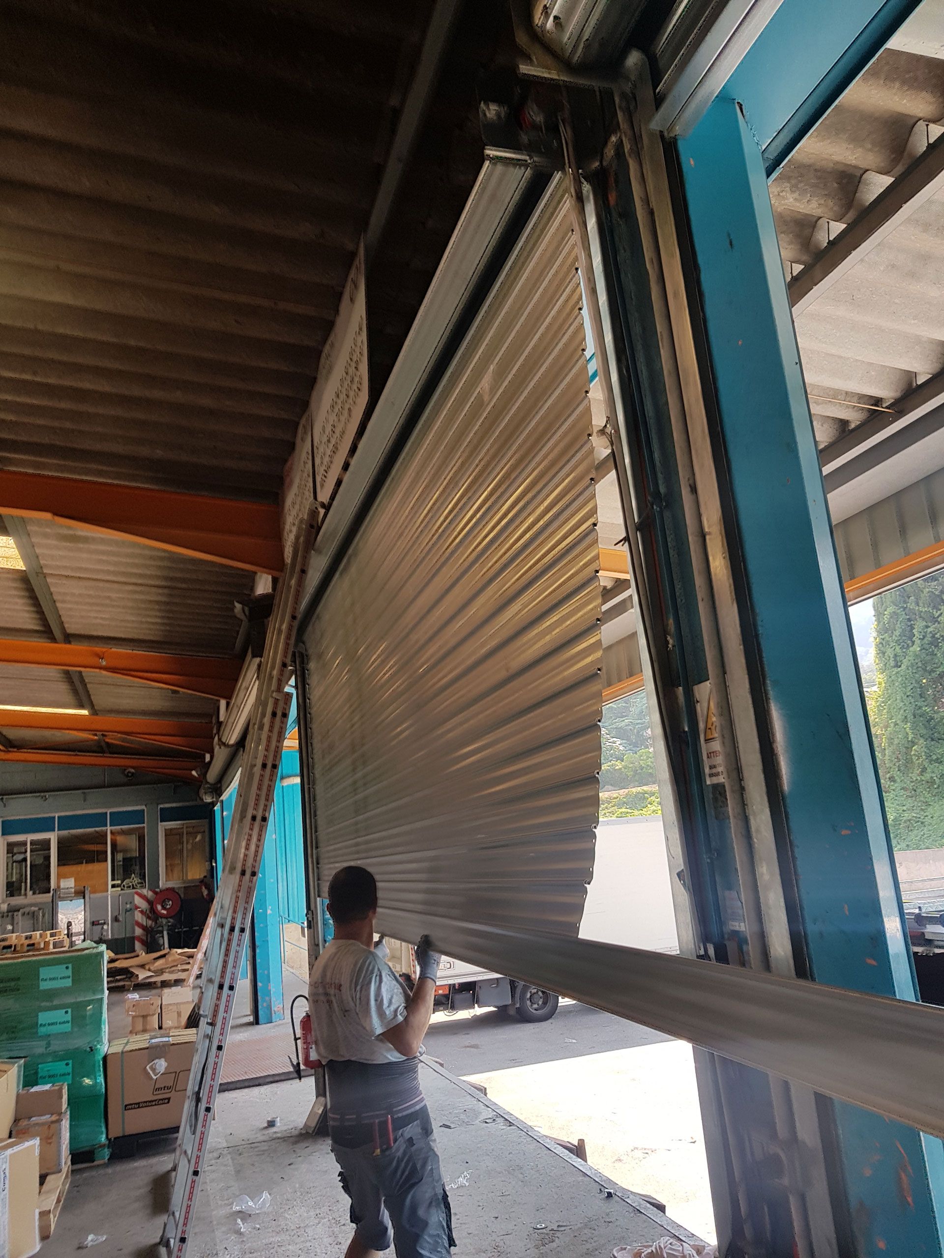 Un homme travaille sur une porte métallique sectionnée partiellement ouverte dans un entrepôt.