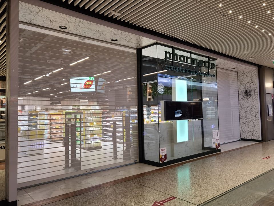 Façade de pharmacie avec volets de sécurité transparents fermés, vue intérieure des étagères et des produits.