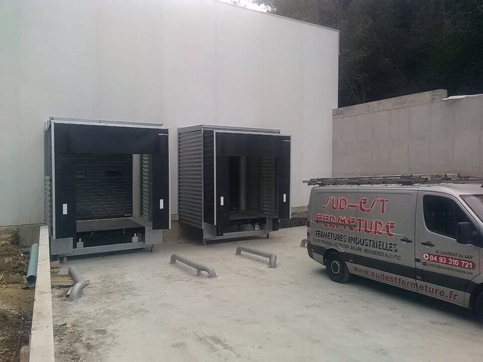 Deux portes de quai de chargement et une camionnette de service stationnées près d'un bâtiment blanc en construction.