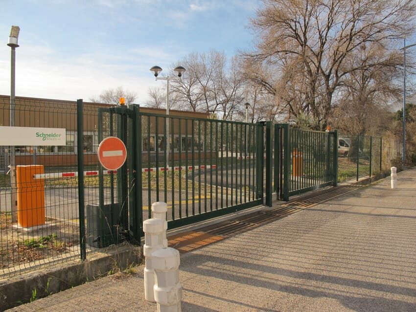 Portail de sécurité vert avec panneau « Entrée interdite », barrière orange et bâtiment industriel.