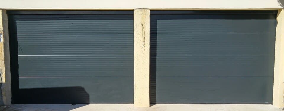 Porte de garage bleu foncé à lignes horizontales, encadrée par des piliers clairs.