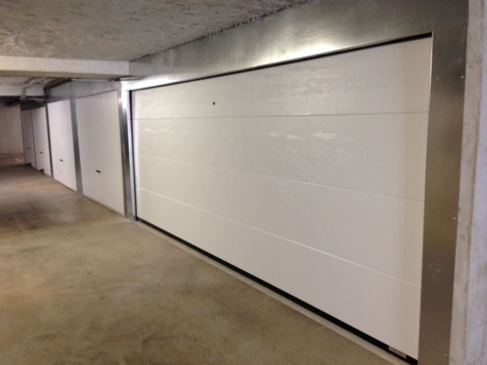 Portes de garage blanches dans un parking en béton.