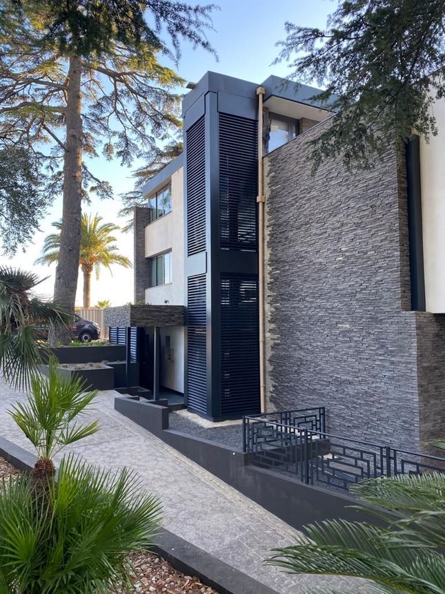 Maison moderne avec façade en pierre et blanche, partie à claire-voie sombre et allée paysagée.