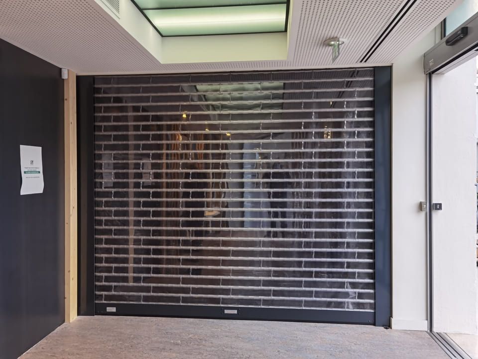 Un rideau métallique de sécurité transparent encadre une porte, laissant entrevoir partiellement l'intérieur.