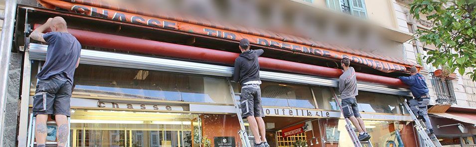 Cinq personnes sur des échelles travaillent sur un auvent d'un bâtiment.