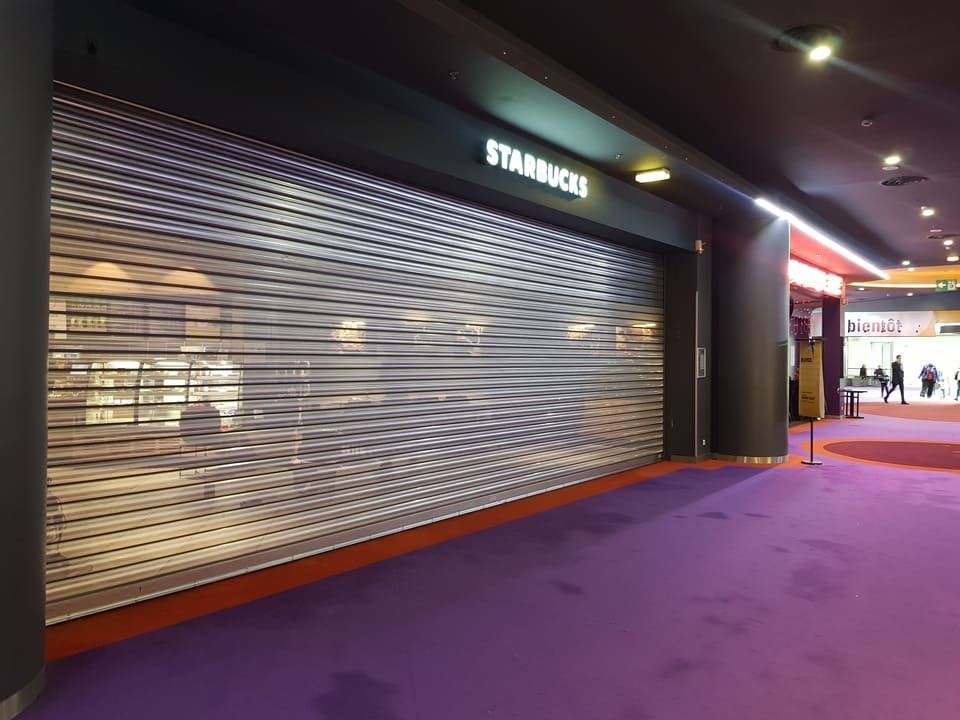 Façade fermée d'un Starbucks, rideau métallique de sécurité baissé. Moquette violette au sol, boiseries orange.