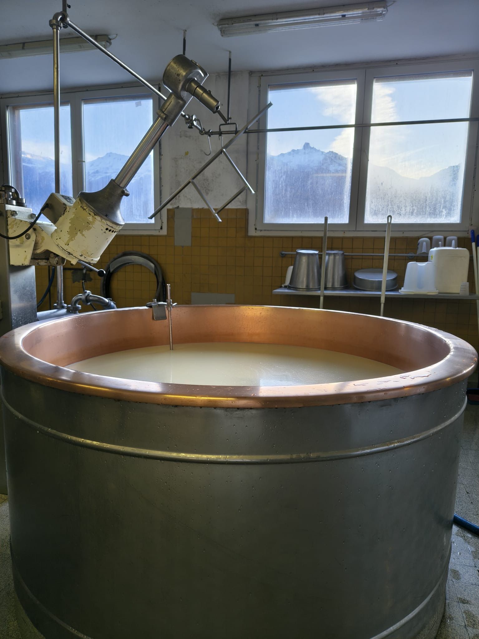 Personne portant des gants noirs coupant du fromage avec une scie à fil sur une table de dégustation ; bouteille de vin rosé.