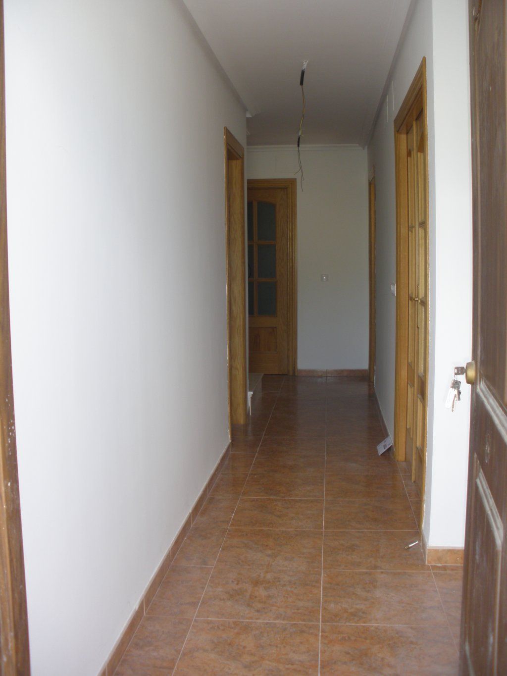 Un pasillo con paredes blancas y suelos de baldosas marrones.