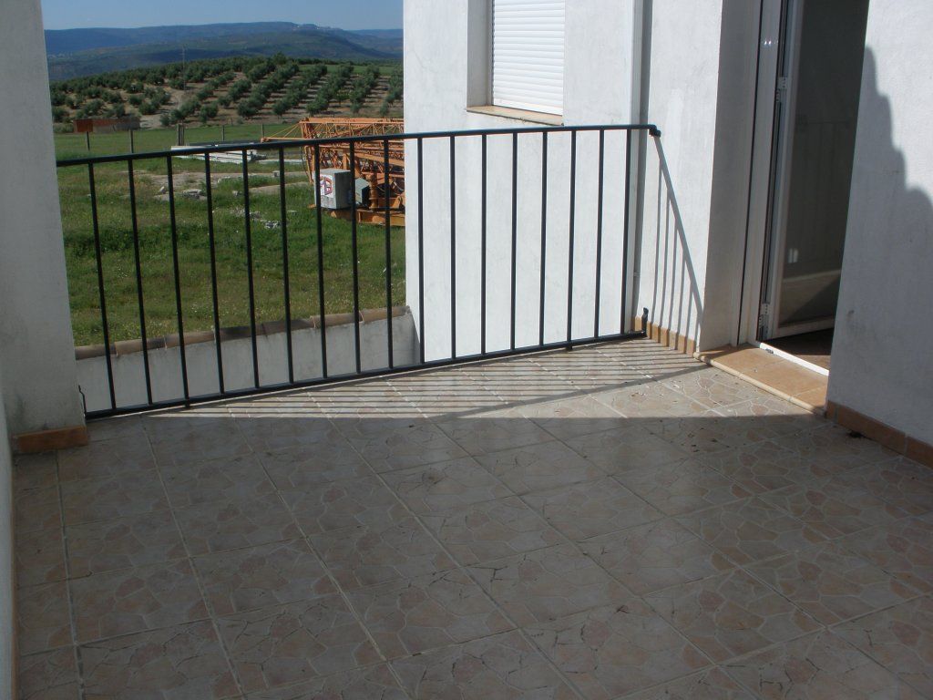 Un balcón con barandilla de metal y vista a un campo.