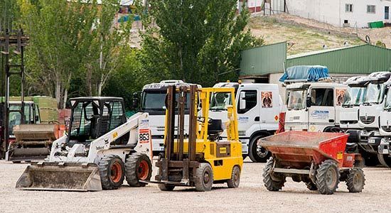 Una fila de vehículos de construcción están estacionados en un estacionamiento.