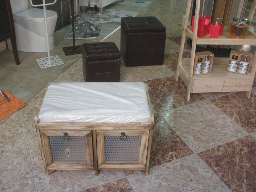 Una otomana de madera se encuentra sobre un suelo de baldosas al lado de un inodoro.