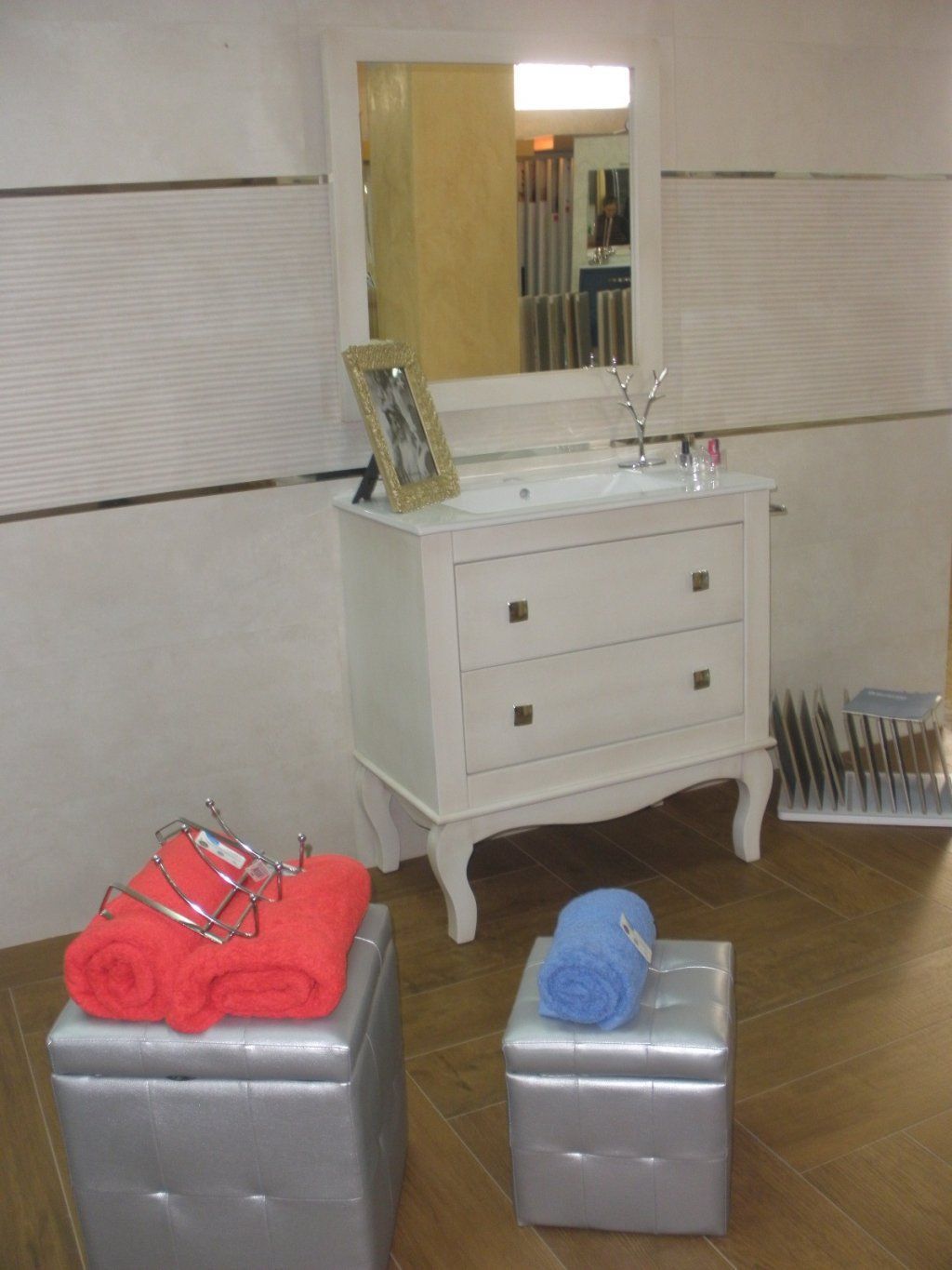 Un baño con lavabo, espejo y dos otomanas.