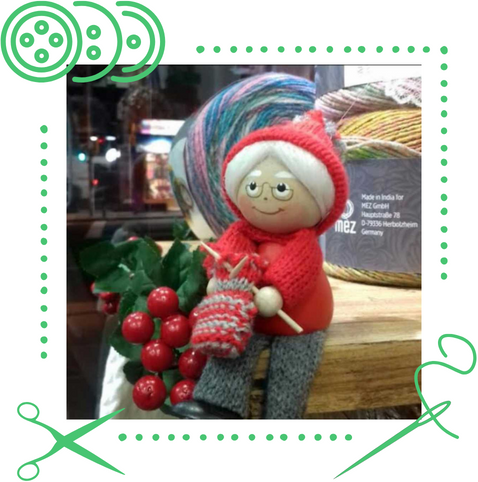 Una muñeca con capucha roja está tejiendo un par de mitones.