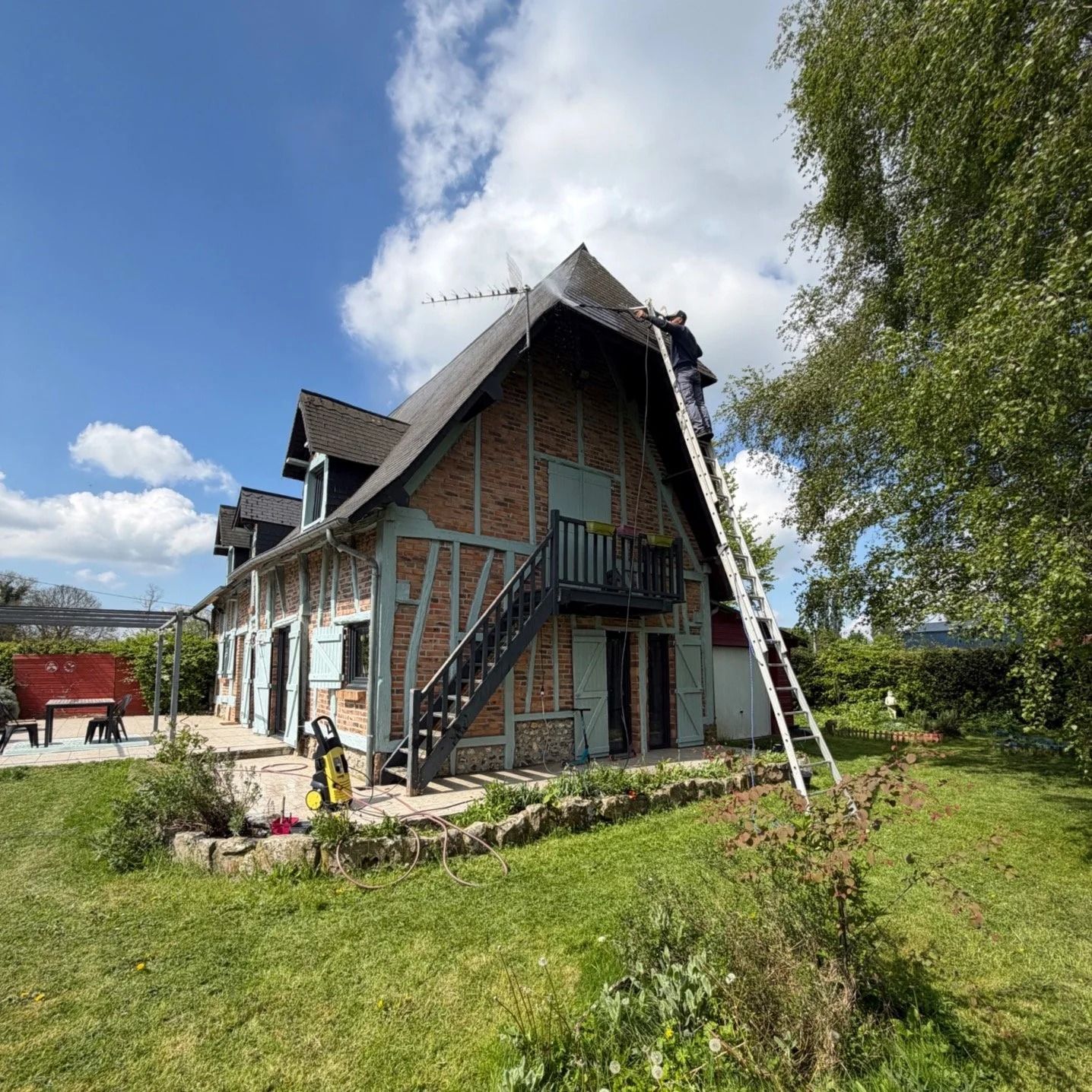 Maison à deux étages en construction avec escalier extérieur, échafaudage et échelle dans une cour gazonnée