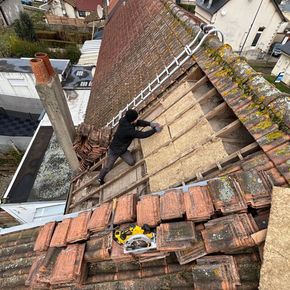 Ouvrier sur un toit pentu, réparant des tuiles à côté d'une échelle et d'outils sur une maison d'habitation.