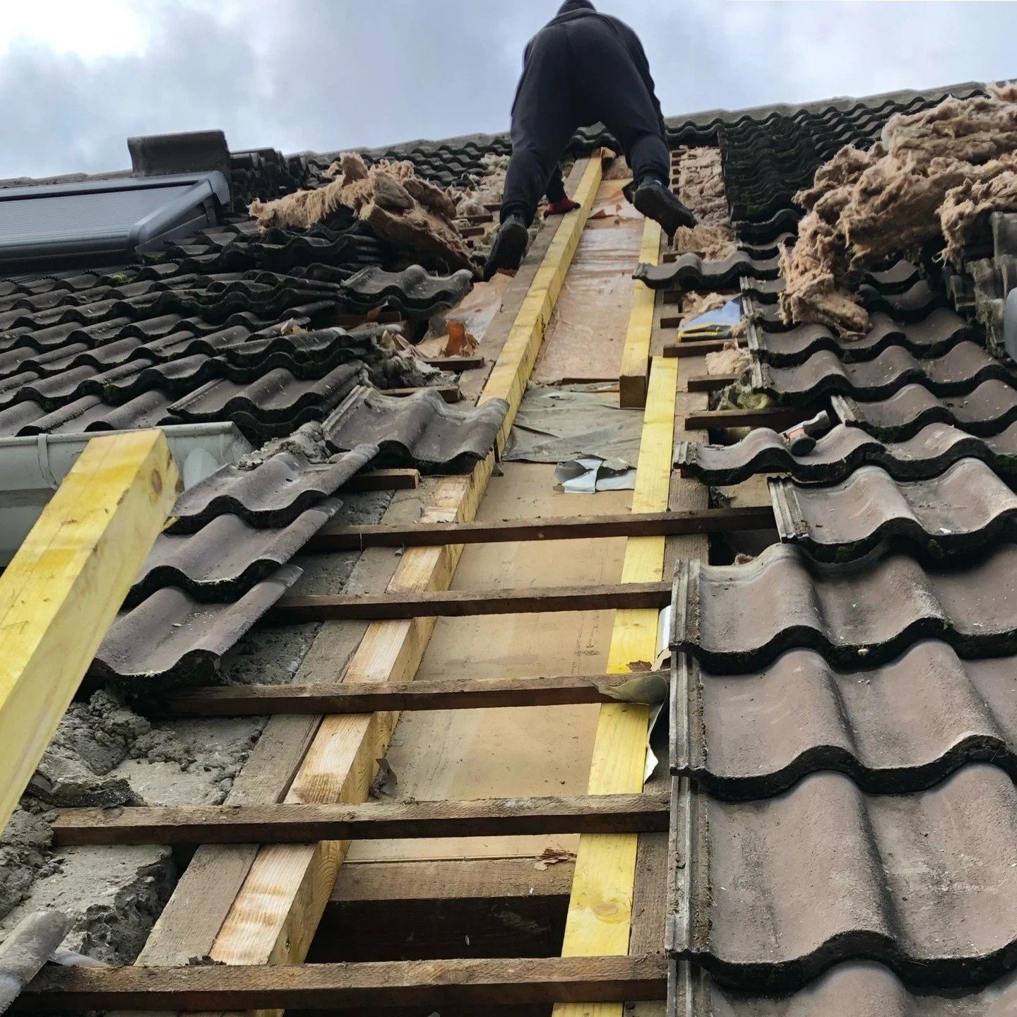 Un ouvrier répare des tuiles endommagées sur un toit, près d'un échafaudage en forme d'échelle.