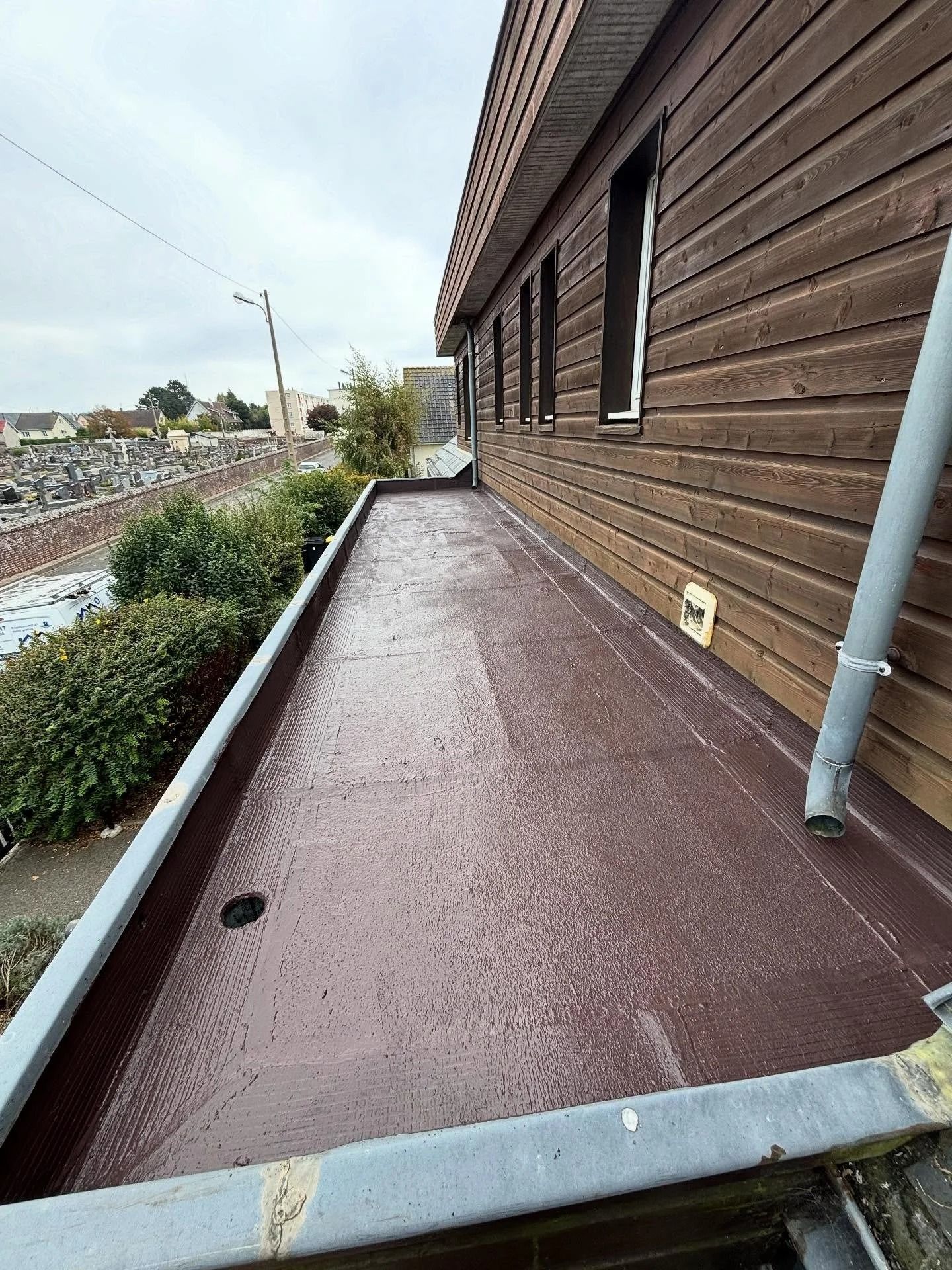 Passerelle étroite sur le toit d'un bâtiment à façade en bois, avec un sol rouge étanche et un tuyau d'évacuation.