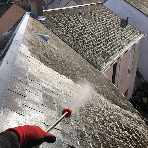 Une personne nettoie un toit en pente au nettoyeur à haute pression avec une buse rouge