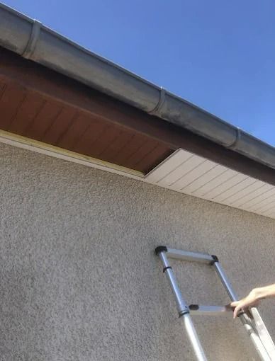 Une échelle appuyée contre le mur en stuc d'une maison, sous l'avant-toit, une main tendue vers elle.