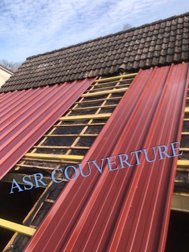 Toiture en tôle rouge en cours de réparation, avec une échelle en bois au sommet et des tuiles sombres au-dessus.