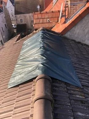 Réparation de toiture avec une bâche bleue recouvrant une ventilation de faîtage sur un toit en tuiles dans une zone résidentielle