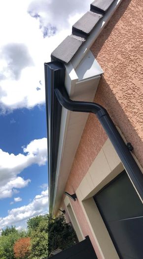 Gros plan sur le bord d'un toit de maison avec une gouttière noire et un soffite blanc sur un ciel bleu nuageux