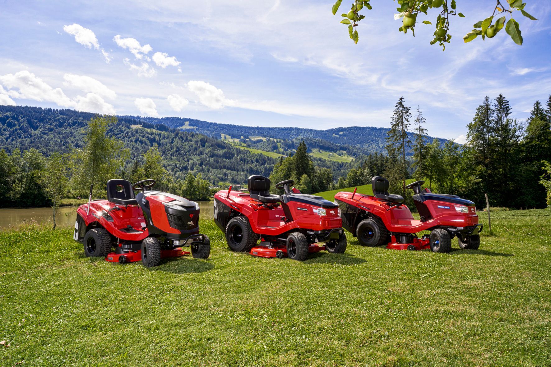 Drei rote Rasenmäher sind auf einer Wiese geparkt.