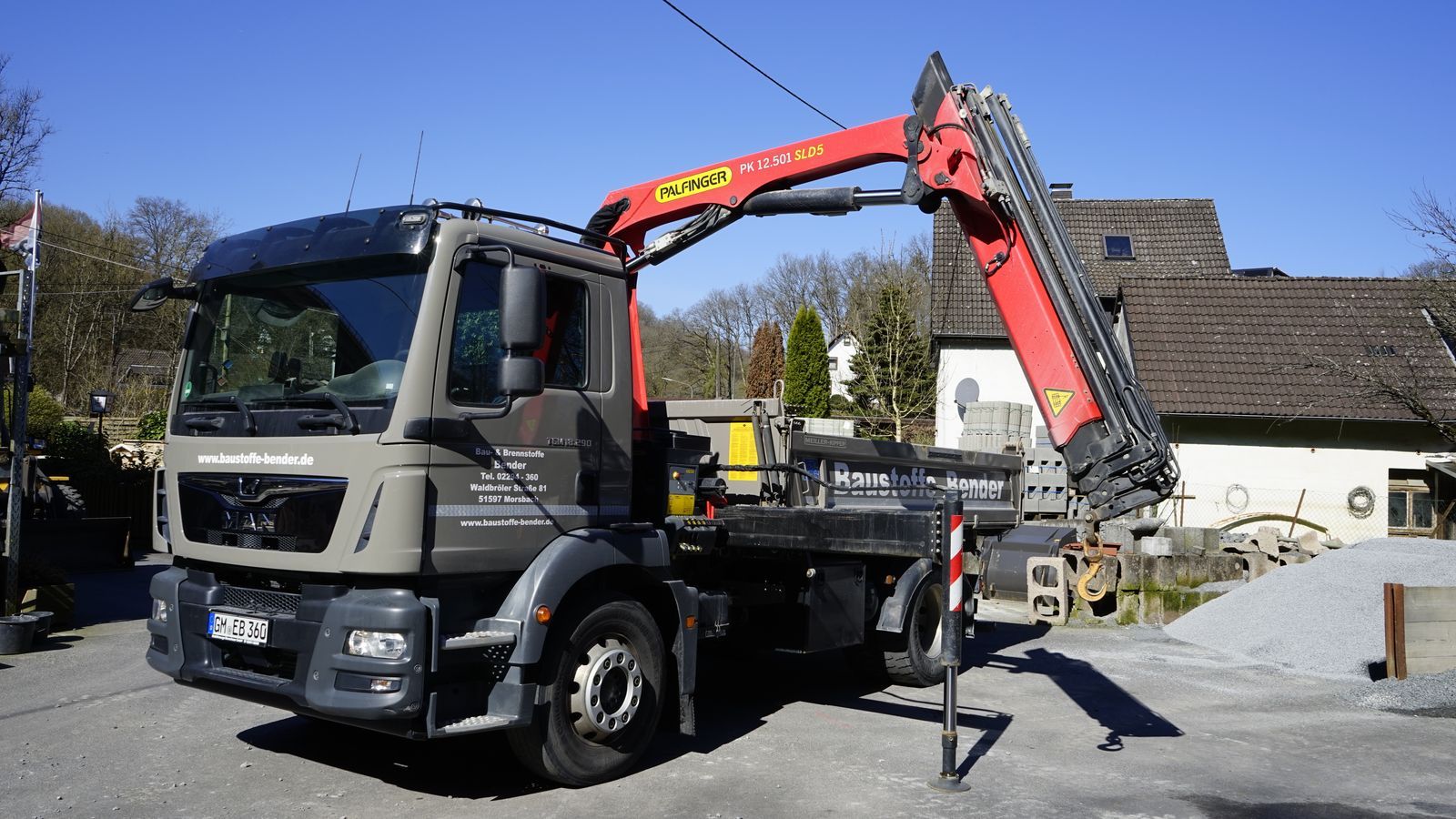 Vor einem Haus parkt ein LKW mit einem daran befestigten Kran.
