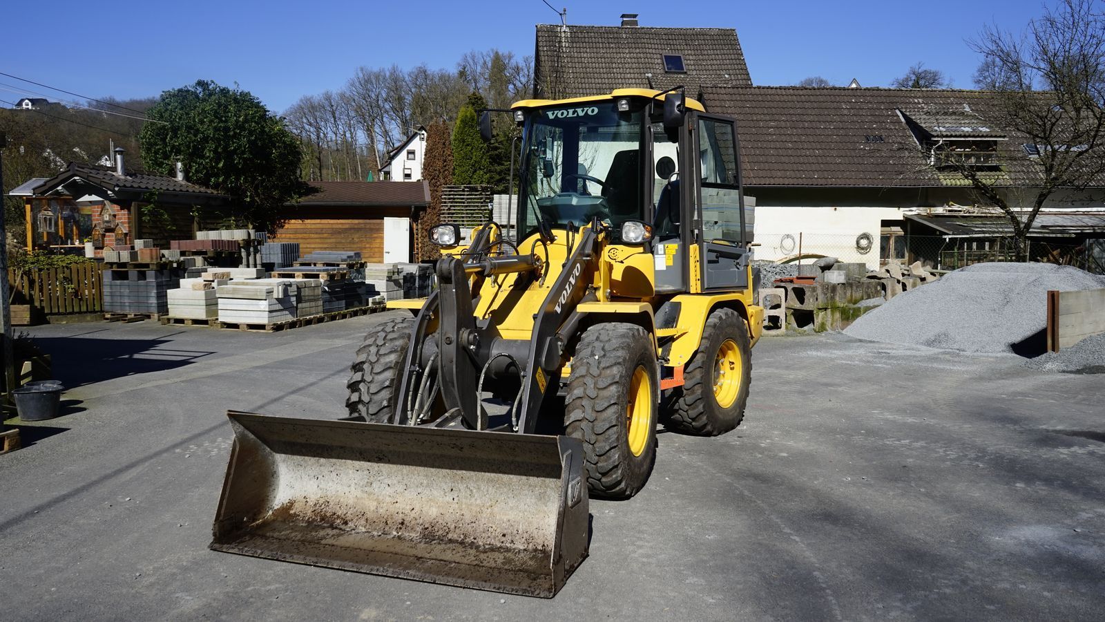 Auf einem Parkplatz vor einem Haus steht eine gelbe Planierraupe.