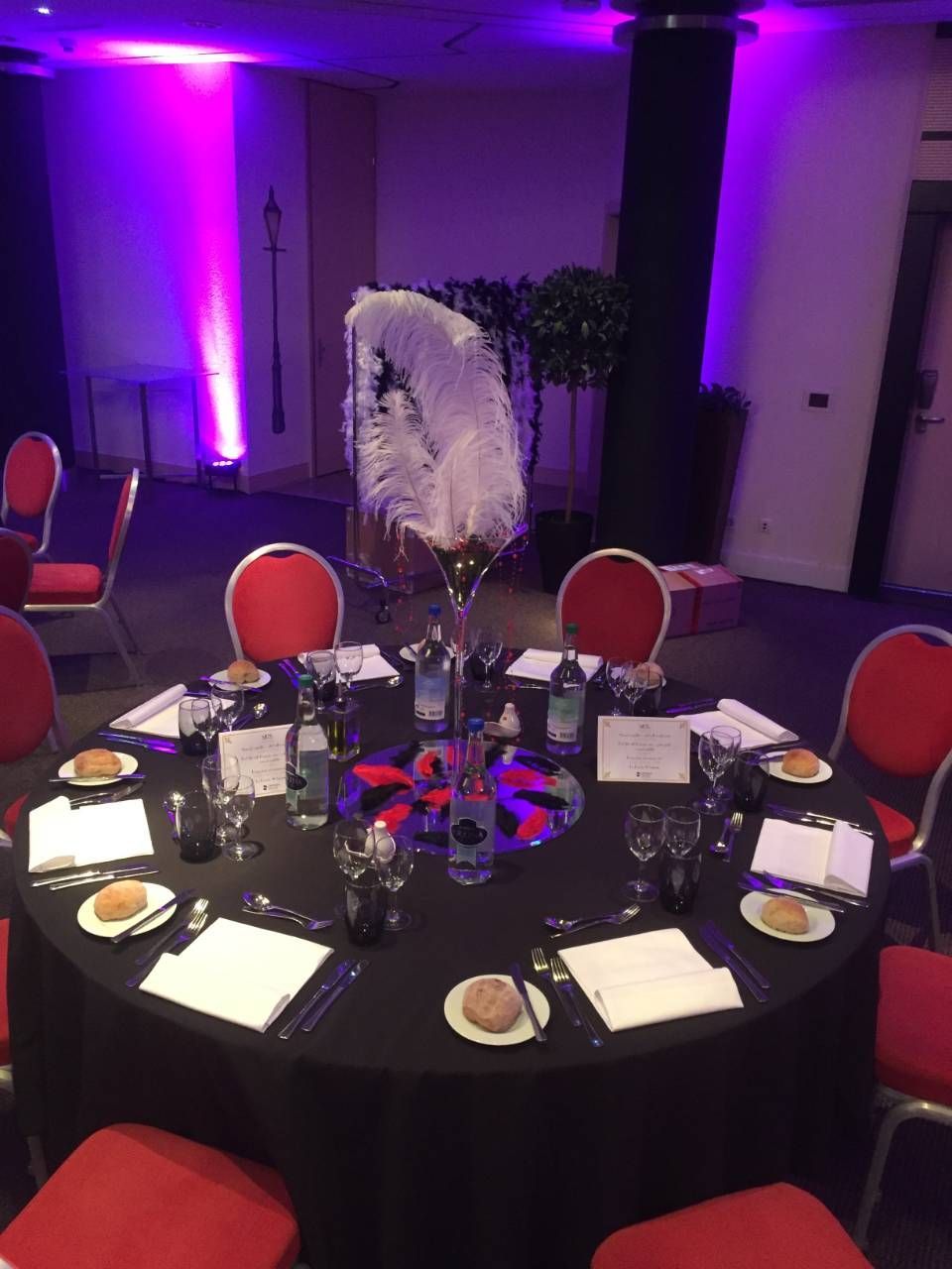 Table ronde de banquet avec des chaises rouges dans une salle de réception éclairée de violet, décorée pour un dîner formel.