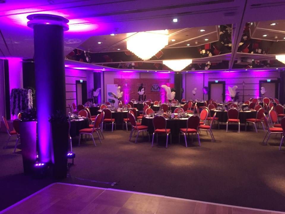 Salle de banquet éclairée en violet, avec tables rondes et chaises disposées pour un événement