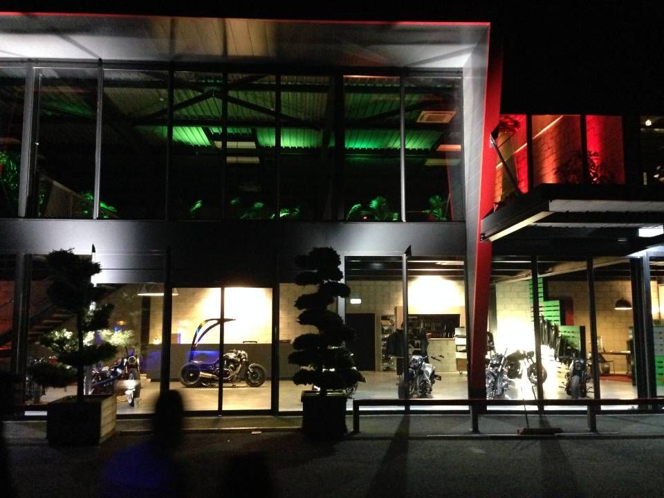 Bâtiment moderne à façade de verre la nuit, avec éclairage vert et rouge et voitures garées à l'intérieur