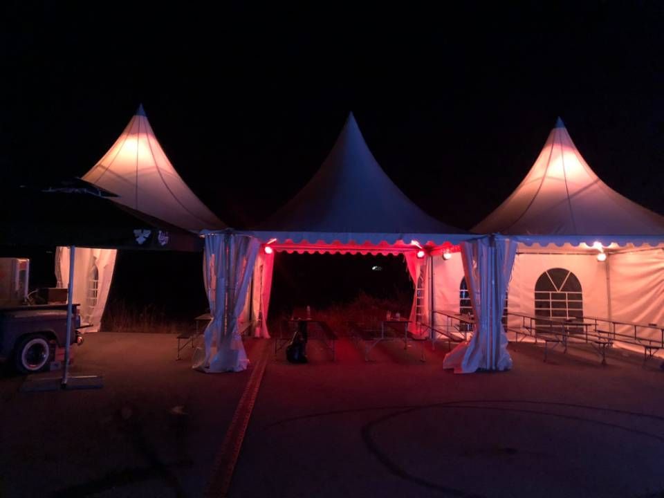 L'entrée de la tente est éclairée la nuit par un éclairage rouge, flanquée de deux tentes blanches pointues.