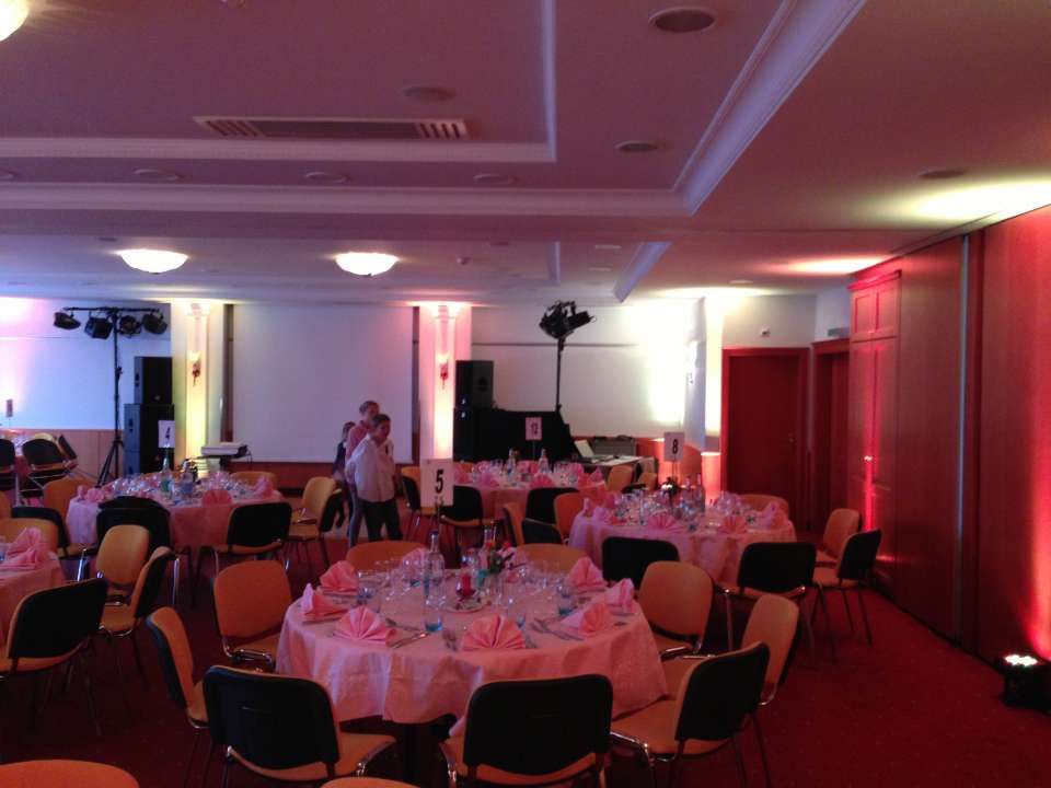Salle de banquet faiblement éclairée, avec des tables rondes dressées pour un événement et un éclairage rouge indirect sur les murs.