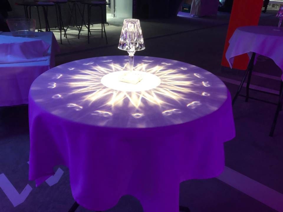 Table ronde éclairée en violet avec un centre lumineux et un petit bougeoir posé dessus, dans un espace événementiel tamisé.