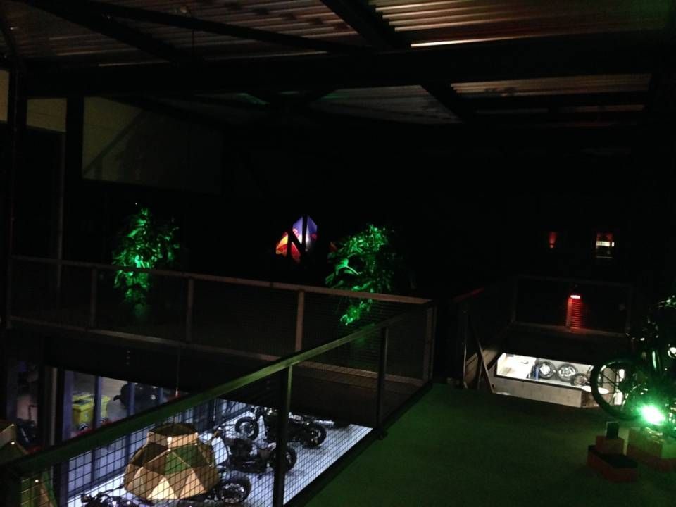 Balcon intérieur tamisé avec plantes éclairées de vert, une rambarde et une petite vitrine éclairée dans une pièce sombre