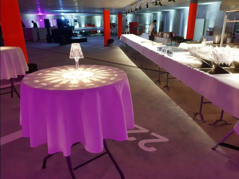 Salle de banquet éclairée en violet, avec table ronde et longs buffets dressés pour un événement