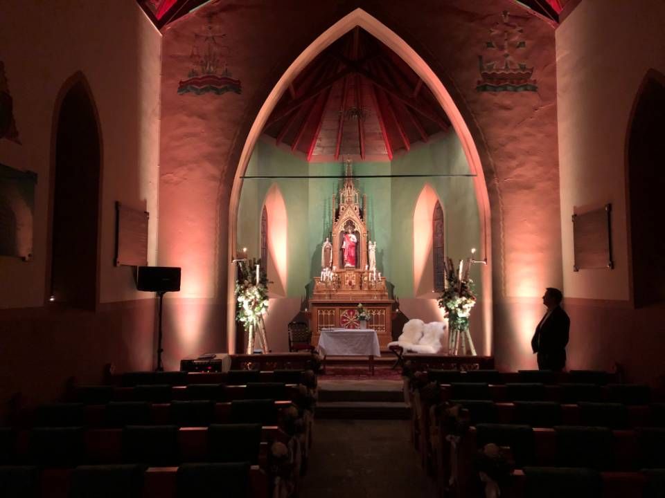Chapelle faiblement éclairée, avec un autel orné, un éclairage rouge et quelques personnes assises sur des bancs.