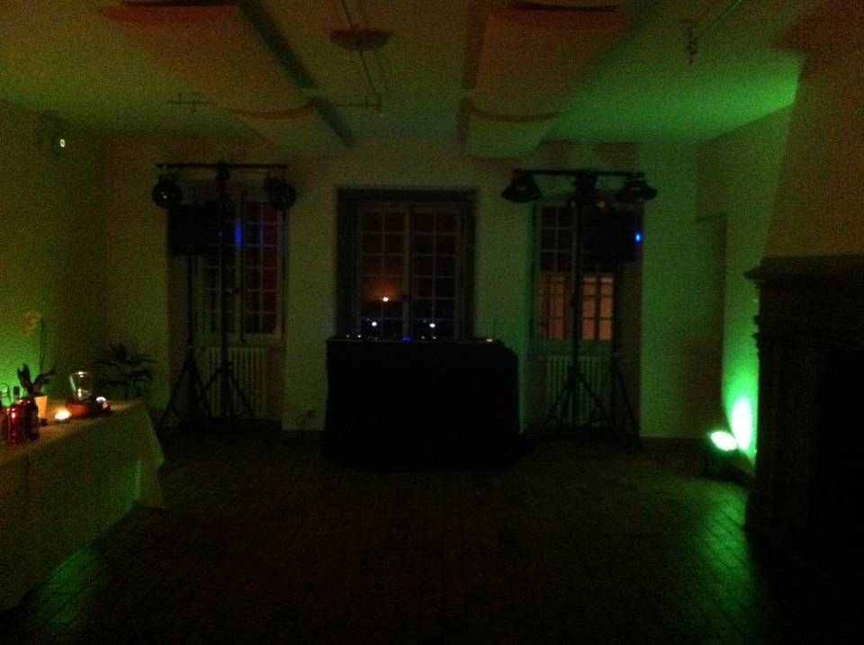 Pièce faiblement éclairée avec des lumières d'accentuation vertes, des tables le long des murs et une cabine de DJ ou un présentoir central.