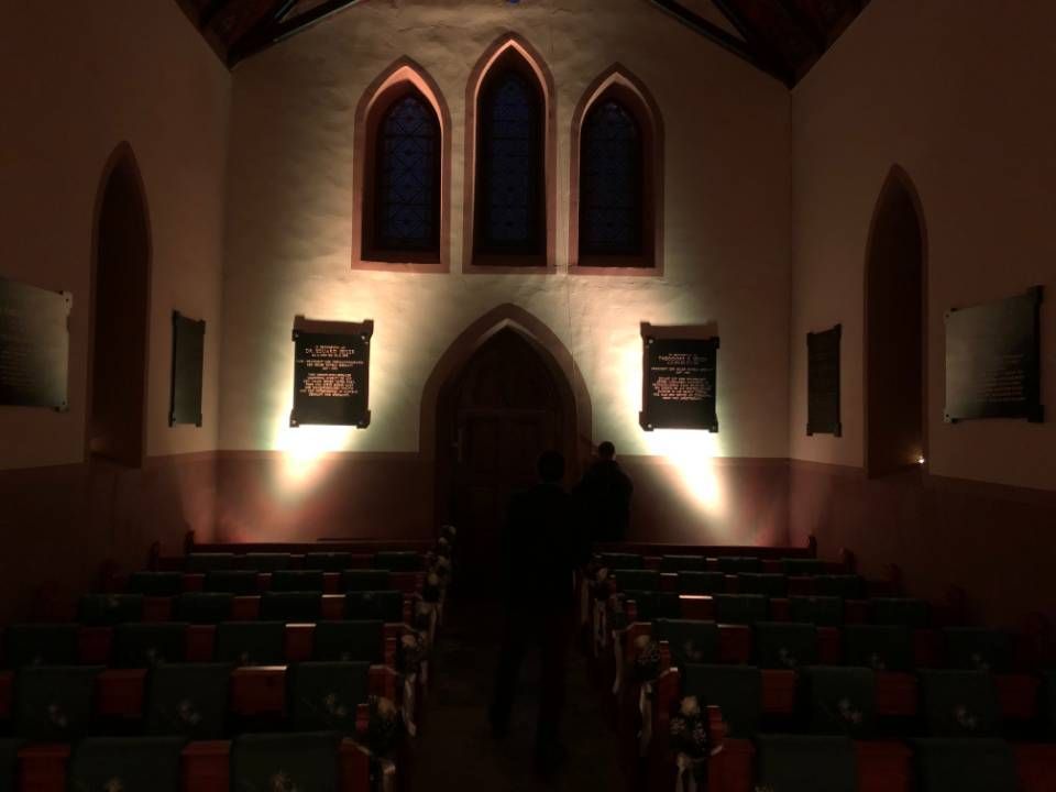 Le sanctuaire de l'église, faiblement éclairé, est orné de rangées de bancs aux coussins rouges et de fenêtres cintrées au-dessus de l'autel.